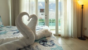 A hotel room with a bed featuring a heart-shaped towel arrangement, a view of the sea through a glass door, and a lamp on the right. - Condado Lagoon Villas/Connected Bayfront Studios w/views, kitchen/washer/dryer (San Juan)