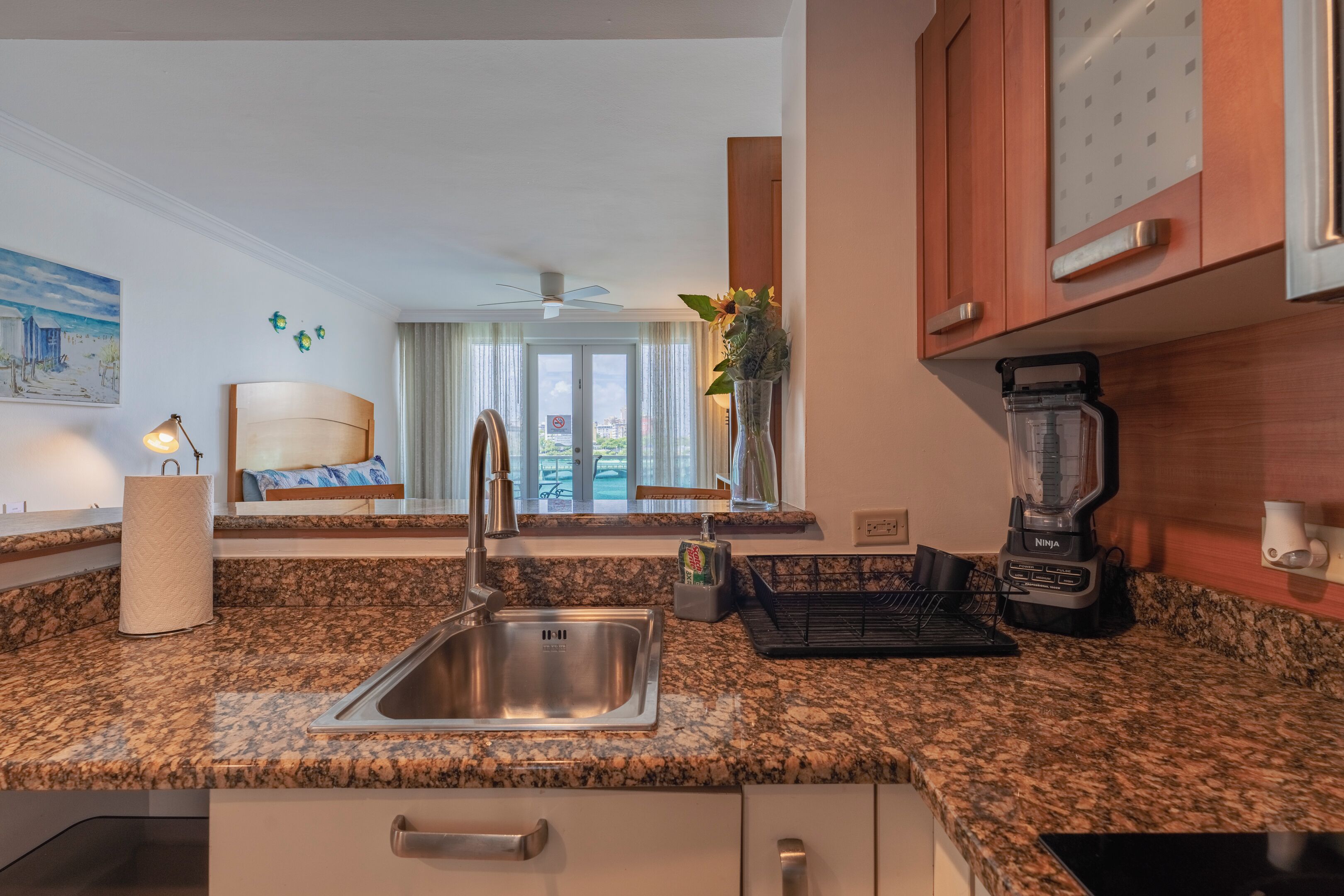A modern kitchen with granite countertops, a stainless steel sink, a blender, and a view of the city through large windows.