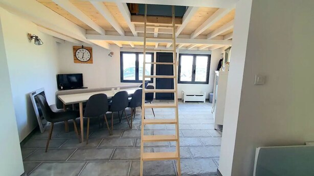 Un interno moderno con zona pranzo, televisore, scala in legno e ampie finestre.