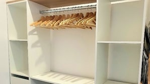 Armadio a muro con scaffali multipli, un appendiabiti in legno e contenitori portaoggetti.