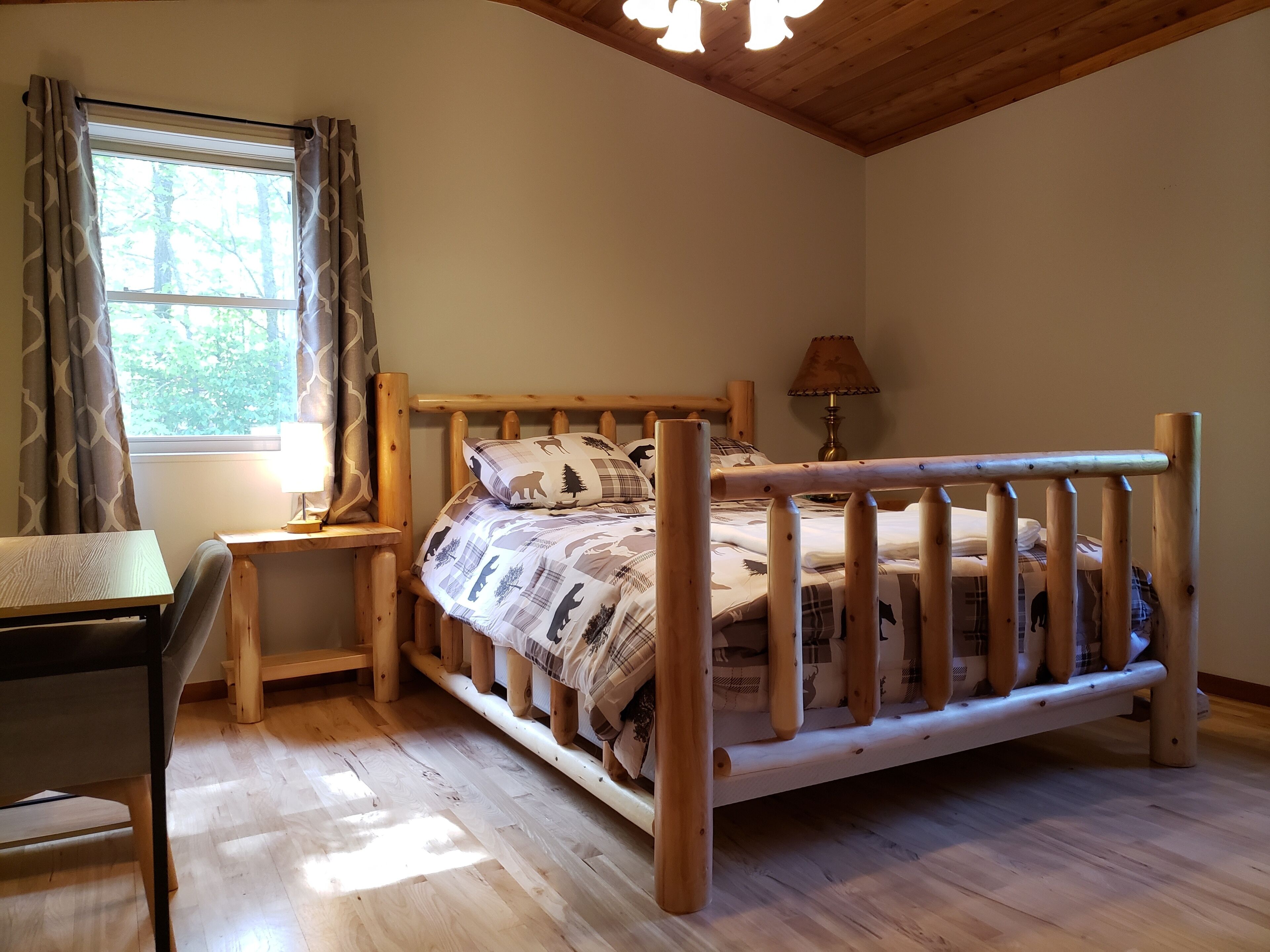 A wooden bed with a headboard, a bedside table, a lamp, and a window with curtains.