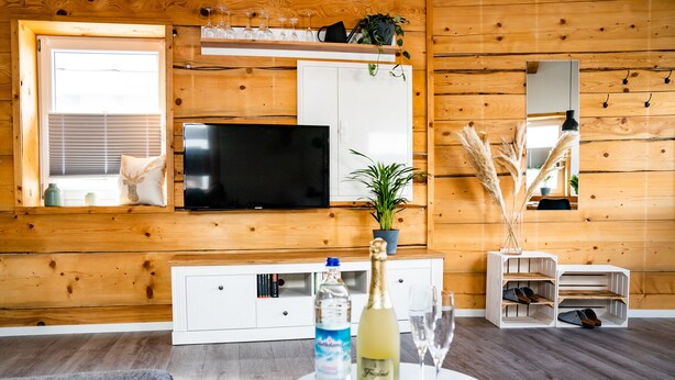 Ein modernes Wohnzimmer mit Flachbildfernseher, einem weißen Schrank, einer kleinen Pflanze, einer Champagnerflasche und einem Schuhregal.
