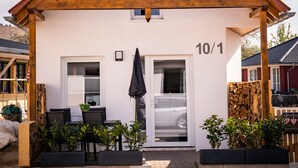 Ein zweistöckiges Haus mit rotem Dach, der Hausnummer '10/1' an der Vorderseite und einer kleinen Außenbereich-Sitzgelegenheit mit Stühlen und Tisch.