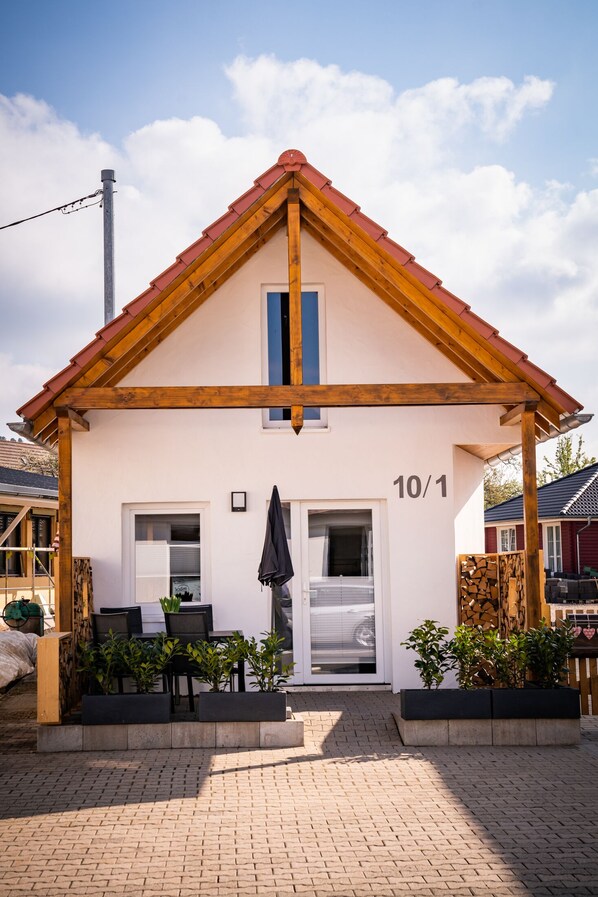 A two-story house with a red roof, a number '10/1' on the front wall, and a small outdoor seating area with chairs and a table.