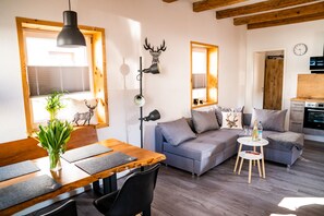 A modern living room with a wooden dining table, grey sofa, and a small white side table.