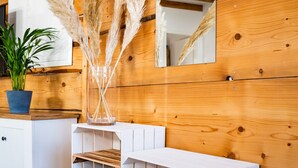 Ein modernes Interieur mit Holzwandverkleidung, einem weißen Konsolentisch mit Spiegel, einer Topfpflanze, Pampasgras und einem Schuhregal.