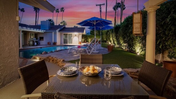 An outdoor patio with a table set for dining, overlooking a swimming pool and a house. - Serene 1 bed Casita w/Pool, Spa & Mountain Views (Palm Springs)