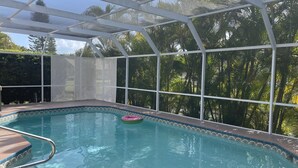 Ein überdachter Pool mit klarem, blauem Wasser, umgeben von einem weißen Zaun und üppiger Bepflanzung.