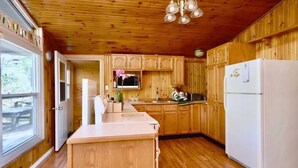 A wooden cabin kitchen with a central island, wooden cabinets, a white refrigerator, and a hanging light fixture.
