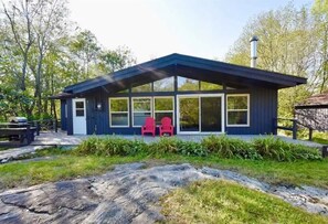 Une cabane moderne dotée de grandes fenêtres, d’un porche abrité et de chaises rouges à l’extérieur.