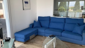 Una sala de estar moderna con un sofá seccional azul, una mesa de centro de vidrio y un televisor de pantalla plana.