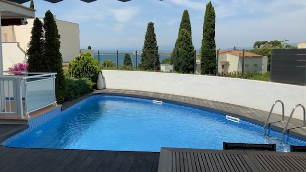 Una piscina con vista al mar, rodeada de vegetación y un área de estar cubierta.