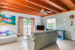 A living room with a ceiling fan, a television, a sofa, and a painting of a fish.