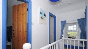 Eine Treppe mit weißen Geländern und blauen Akzenten, die zu einem Raum mit einer Holztür und einem mit Vorhängen drapierten Fenster führt.