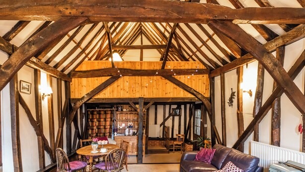 A rustic interior with exposed wooden beams, a dining area with a table and chairs, and a leather sofa. - 2 bedroom accommodation in Coltishall (Coltishall)