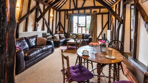 A rustic room with exposed wooden beams, a leather sofa, a wooden dining table, and a view through a window. - 2 bedroom accommodation in Coltishall (Coltishall)