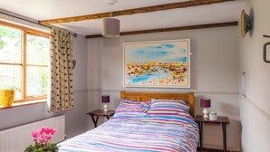 A bedroom with a bed, a window with curtains, a painting on the wall, and a small table with a lamp. - 2 bedroom accommodation in Coltishall (Coltishall)