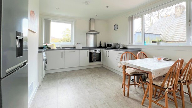 A modern kitchen with white cabinets, a stainless steel refrigerator, a built-in oven, and a dining area with a table and chairs.