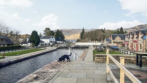 A riverside walkway with a dog, buildings, and a view of hills.