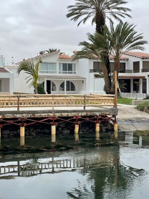 Une propriété située au bord de l’eau, dotée d’un pont, de palmiers et d’un bâtiment blanc avec un toit en tuiles.