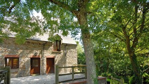 Un edificio de piedra con dos puertas de madera, un camino de grava y una valla de madera.