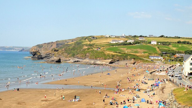 Una playa con gente, tiendas de campaña y edificios al fondo.