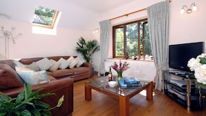 Una sala de estar con un sofá de cuero marrón, una mesa de centro de vidrio, una televisión y una ventana con cortinas.