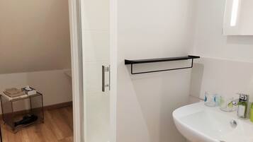 Un baño con lavabo blanco, cabina de ducha de vidrio y toallero.