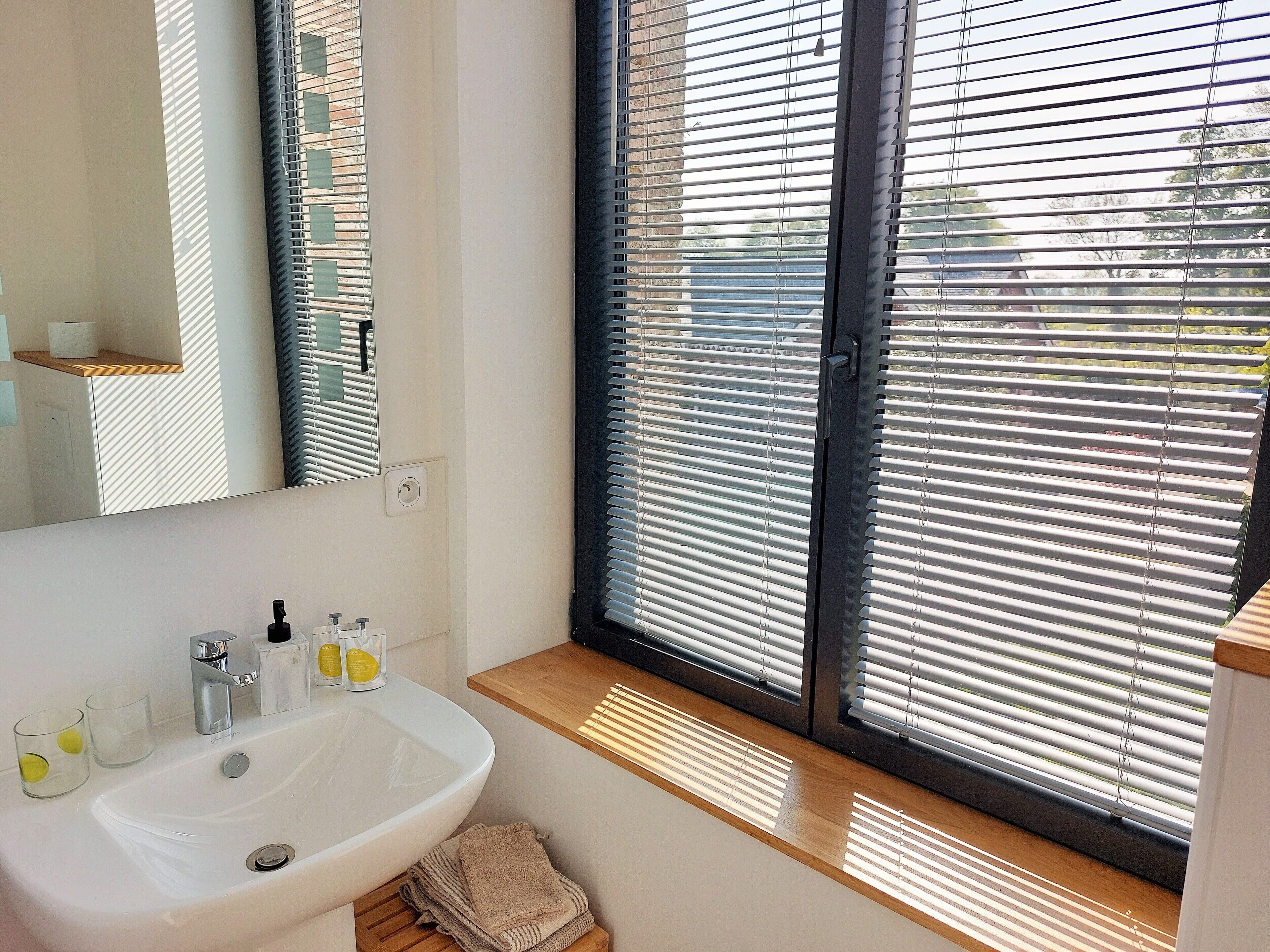 A bathroom with a white sink, mirror, and window with blinds.