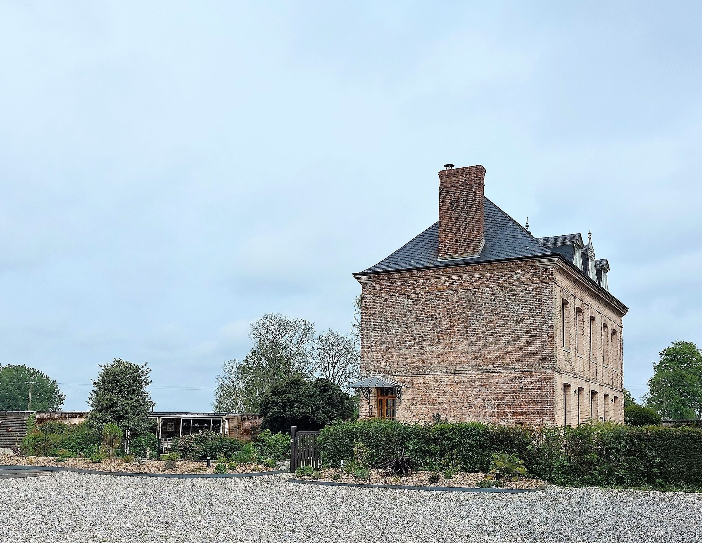 A historic brick building with a prominent chimney, surrounded by gravel and greenery.