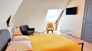 Una habitación con una cama, dos sillas, una mesita, un televisor y una puerta.
