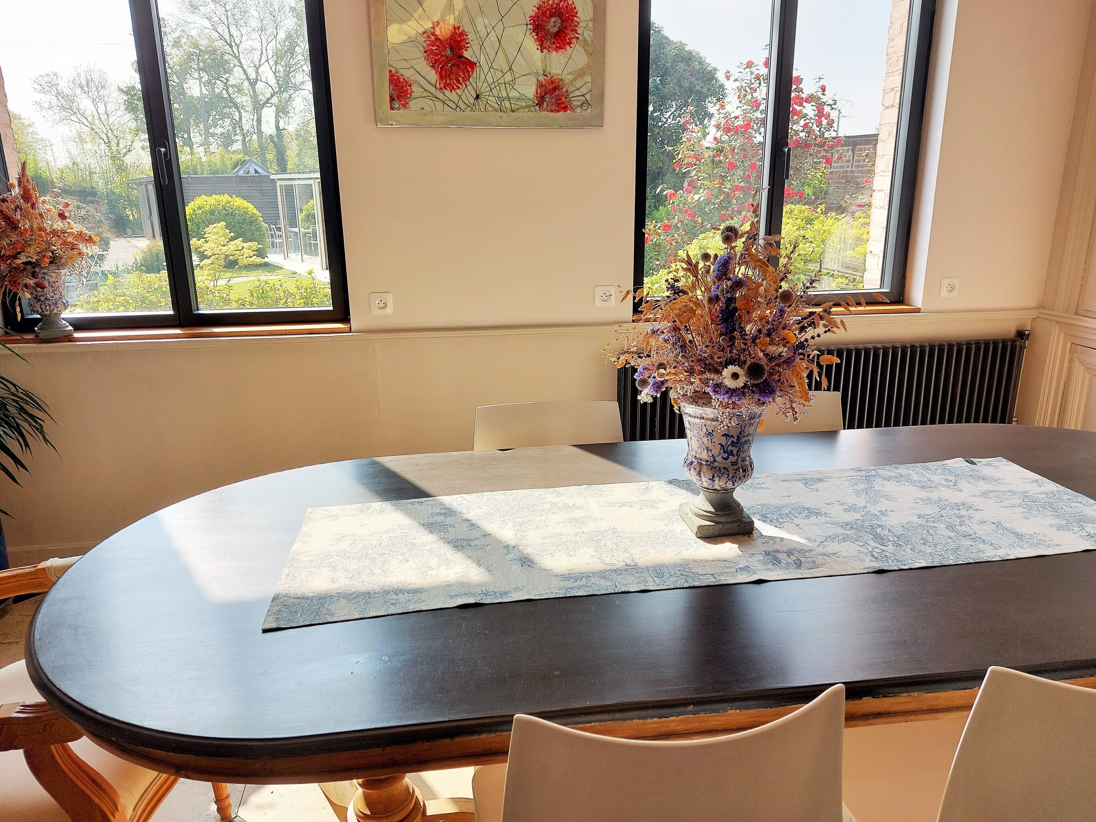 Zona pranzo con tavolo rotondo, sedie, un vaso con fiori e una finestra vista esterna.