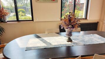 Zona pranzo con tavolo rotondo, sedie, un vaso con fiori e una finestra vista esterna.