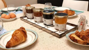 Una mesa de desayuno con croissants, huevos y frascos de mermelada.