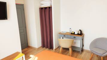 Une petite pièce, bien rangée, avec un bureau en bois, une chaise, un lit et un téléviseur fixé au mur.