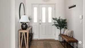 A hallway with a white door, a bench, a lamp, a hanging light fixture, and a wall-mounted coat rack.