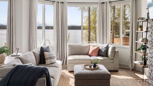 A modern living room with a large window offering a view of a lake and trees.