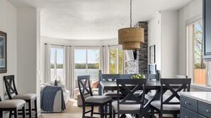 A dining area with a stone fireplace, large windows with a view of a lake, and a hanging wicker light fixture.