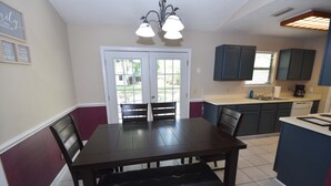 Un comedor con una mesa y sillas de madera oscura, un banco, una cocina con armarios oscuros, una ventana y una puerta que da al exterior.