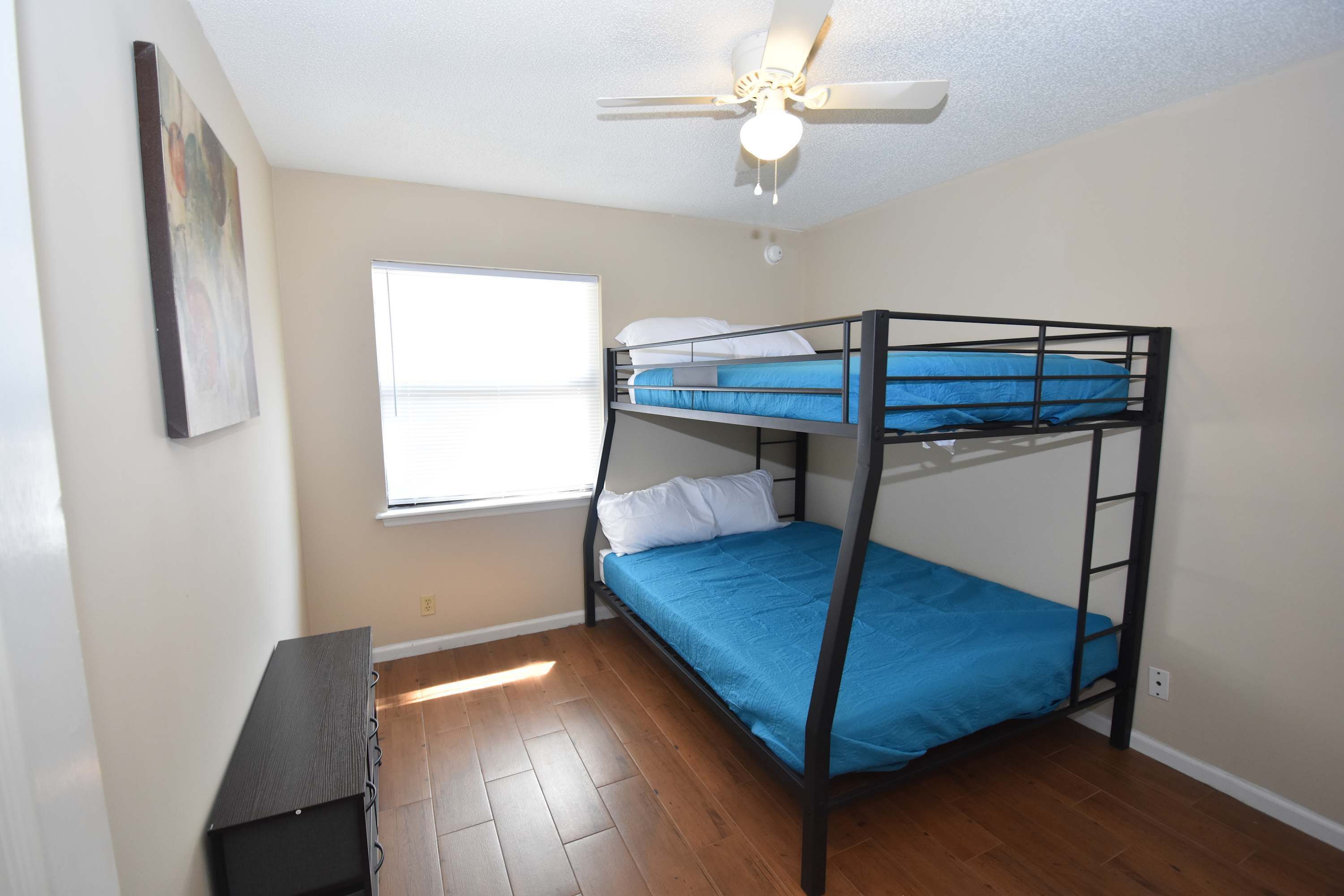 A bunk bed room with a ceiling fan, a window, and a desk.