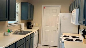 Una cocina compacta con armarios azul oscuro, un refrigerador blanco, una estufa y una ventana con persianas.