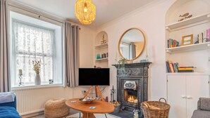 A cozy living room with a fireplace, a television, a bookshelf, and a comfortable seating area. - Y Tŷ Glas is a charming terraced cottage in New Quay. (New Quay)