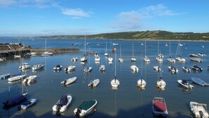A marina with various boats docked, a rocky breakwater, and a clear blue sky. - Y Tŷ Glas is a charming terraced cottage in New Quay. (New Quay)