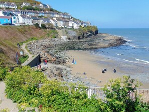 A coastal town with terraced houses, a rocky beach, and a clear view of the sea.