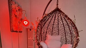 Une pièce avec un fauteuil suspendu, une petite table avec des verres et une bouteille, et un luminaire fixé au mur.