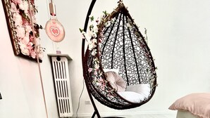 Une pièce comprenant un fauteuil suspendu, un pouf rond, un radiateur et un miroir fixé au mur.