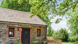 A stone house with a tiled roof, a black door, and two windows. There are potted plants in front of the windows. - 1 bedroom accommodation in Buckland Brewer, near Bideford (Buckland Brewer, near Bideford)