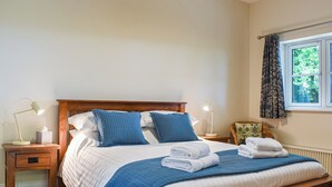 A neatly made bed with blue and white bedding, a wooden headboard, and a nightstand with a lamp and a tissue box. - 1 bedroom accommodation in Buckland Brewer, near Bideford (Buckland Brewer, near Bideford)