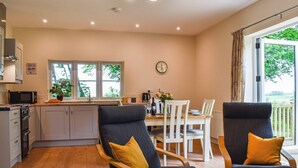 A modern kitchen with a dining area, wooden chairs with yellow cushions, and a view of greenery outside. - 1 bedroom accommodation in Buckland Brewer, near Bideford (Buckland Brewer, near Bideford)