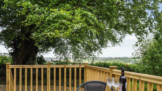 A wooden deck with a glass table and chairs, a bottle of wine, and a bowl of macaroni salad. - 1 bedroom accommodation in Buckland Brewer, near Bideford (Buckland Brewer, near Bideford)